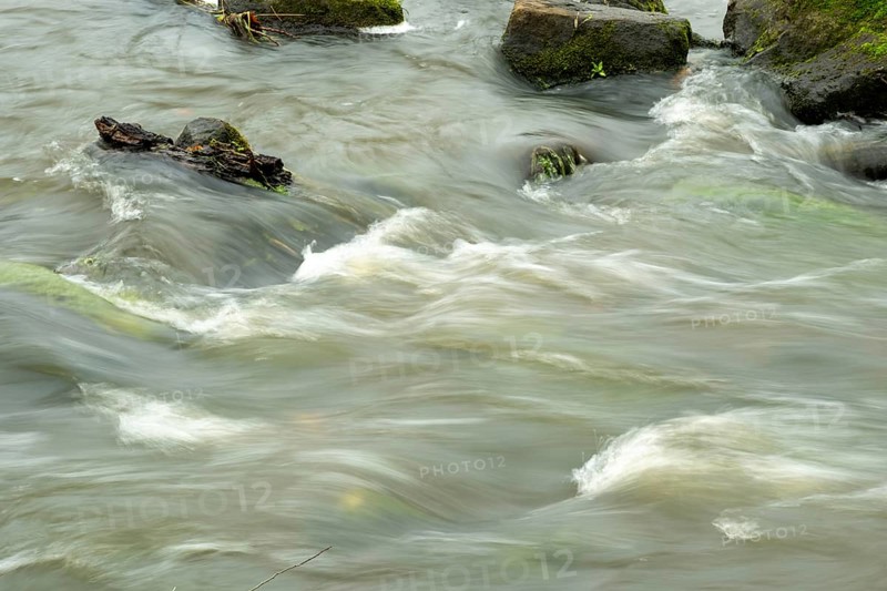 Borken-Hoxfeld, NRW, Germany, A river moves swiftly over stones, creating gentle ripples and currents in a natural setting. The scene is calm with a multitude of rocks partially submerged in water