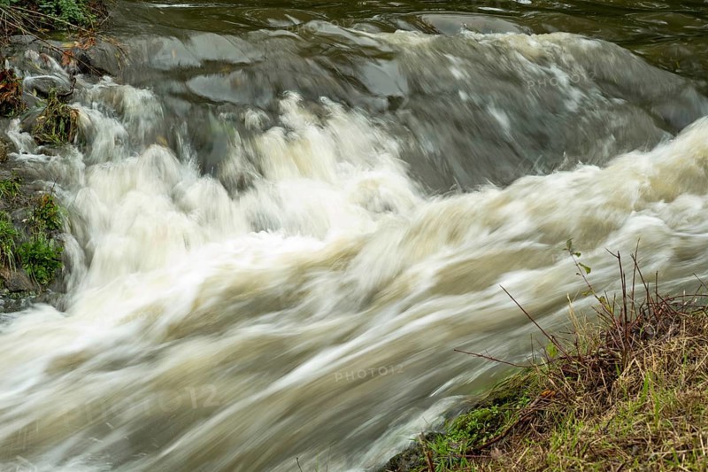 Borken-Hoxfeld, NRW, Germany, Rushing water flows over rocks in a serene natural area, surrounded by lush greenery. Sunlight reflects off the surface, creating a peaceful atmosphere