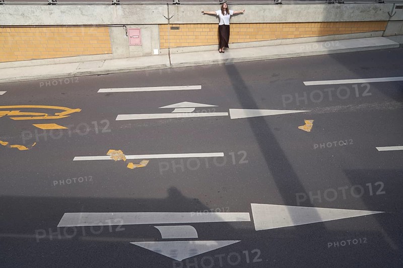 Feeling contrast of light and shadow on the street as metaphor for construction dilemma of warm and hot and cold temperatures in city and traffic design and the used building fundaments sustainability, taking a break, getting a way from it all, feeling inner balance Equilibrium of what one is used to in daily life, conflicted tension, dichotomy, discord, discrepancy, quandary, rifted, mental rift, cleavage, problem, exhaustion, expelled, outcast, exhausted, arms outstretched, urban design materials, sunny weather, resting, lonely, in Magdeburg, Saxony-Anhalt, Germany