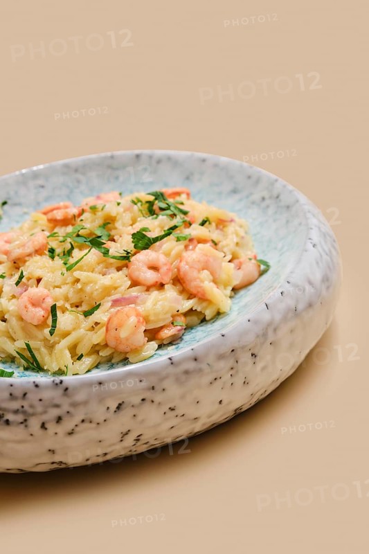 A delicious dish of risoni pasta is topped with tender shrimps and sprinkled with fresh herbs. This comforting meal is perfect for lunch or dinner, served in a charming rustic bowl