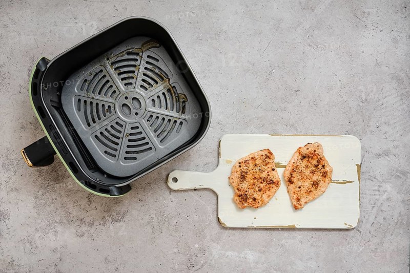 Two perfectly cooked pork sirloin chops rest on a cutting board beside an air fryer basket. The cutlets are seasoned and golden brown, ready to be served as a delicious and easy meal