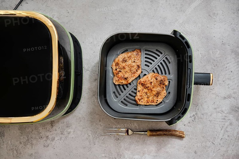 Two cooked seasoned pork sirloin cutlets in the basket of an air fryer. The kitchen setting highlights the convenience of preparing a tasty dish quickly and easily