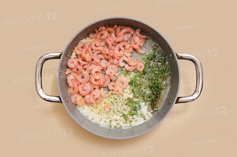 Shrimps and herbs sizzle in a pan, blending with chopped garlic, ginger and olive oil. Process of infusing food with aroma and scents