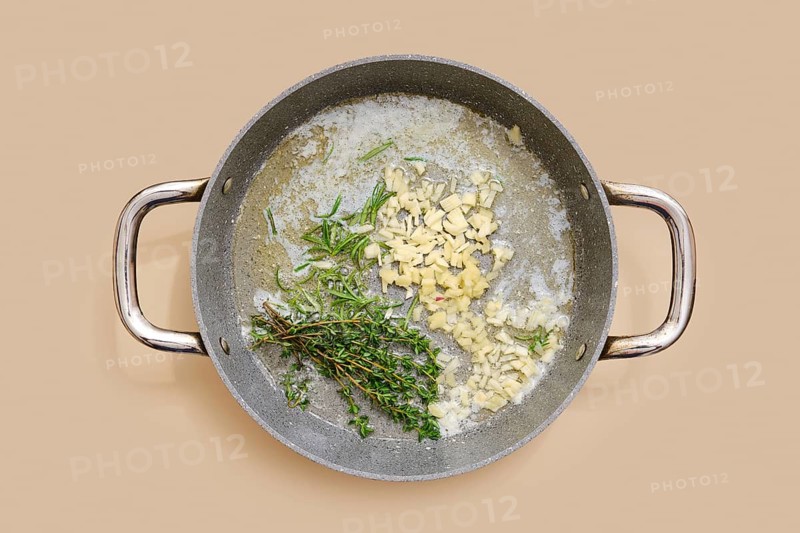 Butter and olive oil are heating in a pan with finely chopped garlic, ginger and fresh thyme and rosemary. The fragrances blend together, creating a rich base for various dishes