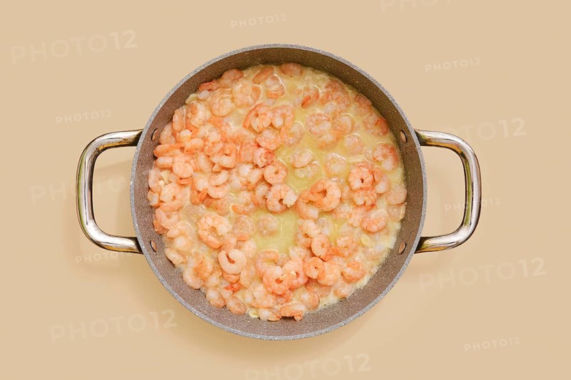 A skillet is filled with juicy, cooked shrimp in a creamy garlic sauce, ready to be tossed with pasta. This dish offers rich flavors perfect for a comforting dinner at home