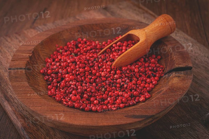 Bright red peppercorns, in a wooden bowl, with a small wooden tray