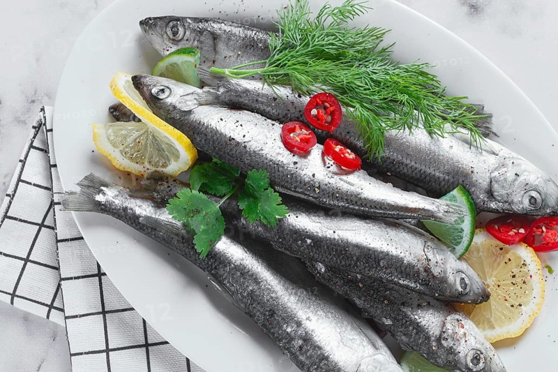 Fresh Herring fish, ready to cook, with herbs and spices, on a white platter, in the kitchen