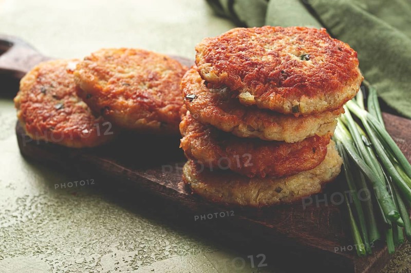 Crispy potato pancakes Latkes, stacked on a wooden board next to fresh green onions, natural light, homemade, no people