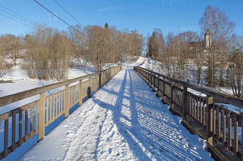 Old wooden walk bridge over river Koskenkylänjoki on a sunny winter day with snow covering the ground, Koskenkylä, Finland