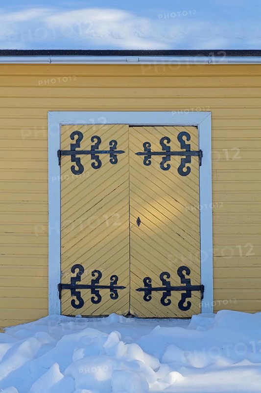 Old wooden double doors with wrought iron decorative hinges in winter with snow on the ground, Suurikylä, Finland