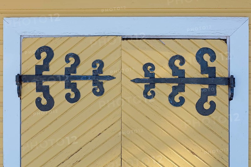 Closeup of old wrought iron decorative hinges on yellow painted wooden doors, Suurikylä, Finland