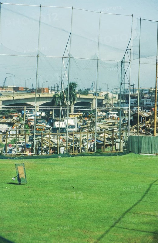 Green lawn of a sports field, slums behind it, Manila in 1995, Philippines
