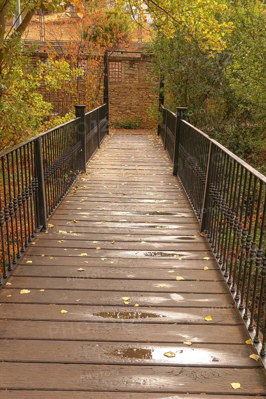 Wooden plank bridge extending through a park with autumn foliage, wet from recent rain, with scattered yellow leaves in setenil de las bodegas cadiz, spain