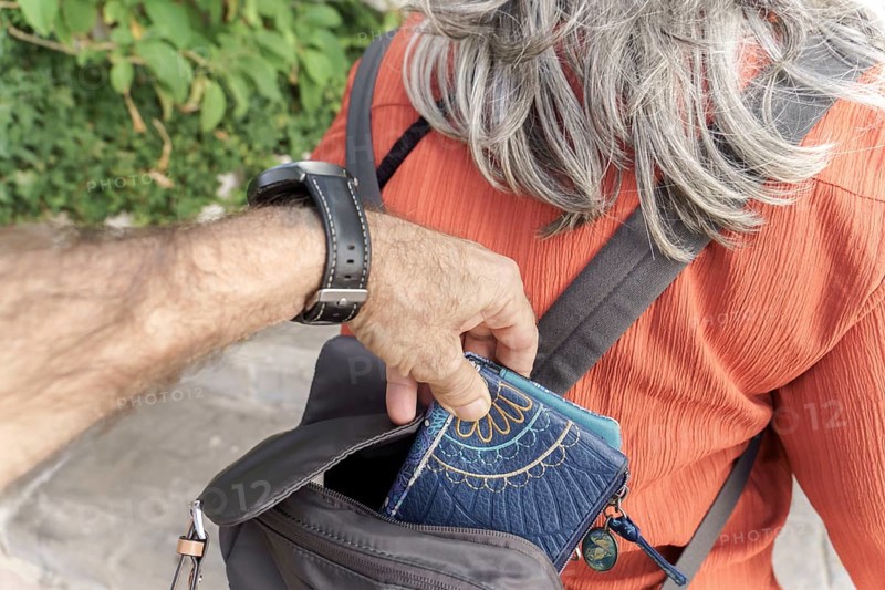 Ronda, malaga, spain Hand of a pickpocket discreetly removing a wallet from a person's backpack, representing theft and street crime