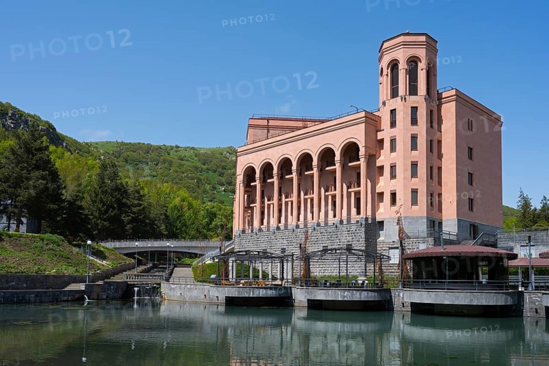 Large pink building with pillars on a river with a bridge surrounded by green hills and clear sky, Hotel Grand Resort Jermuk, Jermuk, health resort, Vayots Dzor province, Armenia