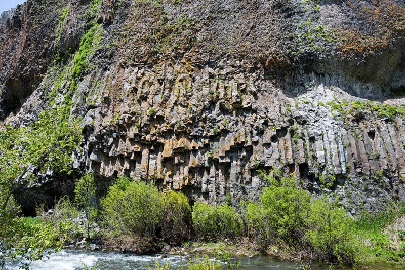 An impressive formation of basalt columns rises above a river surrounded by vegetation, basalt on the Arpa River, Jermuk, Jermuk, Vayots Dzor Province, Armenia