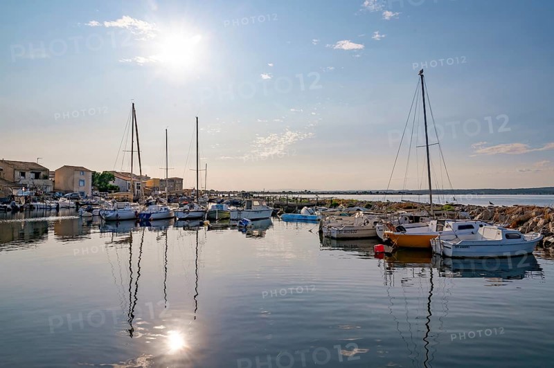Atmospheric sun reflection on the quiet water surface of the harbor basin in La Pointe Courte, seen from the terrace of the Nene restaurant, with fishing boats, sailboats and the neighborhood houses in the background with a view of the Etang de Thau in Sete, Herault department, Occitanie region, France