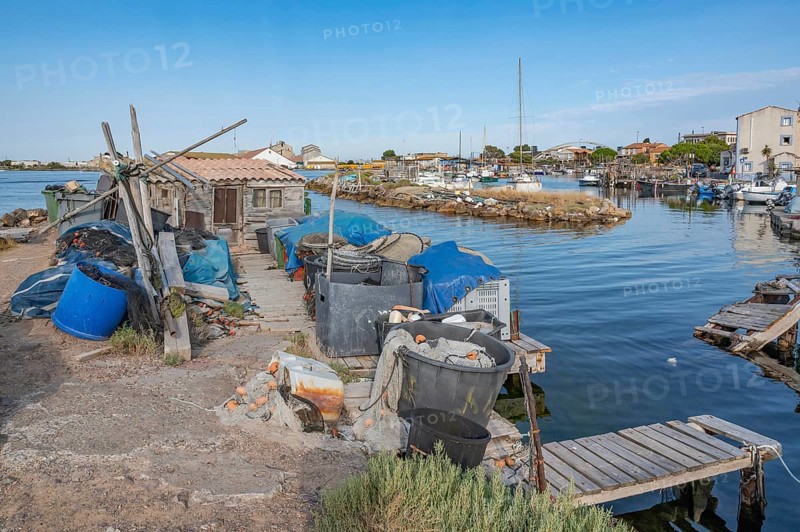 The traditional fishing port of La Pointe Courte with a small wooden shed, fishing nets, baskets and fishing gear on a narrow pier with wooden walkways and boats in the background under a clear blue sky in Sete, Herault department, Occitanie region, France