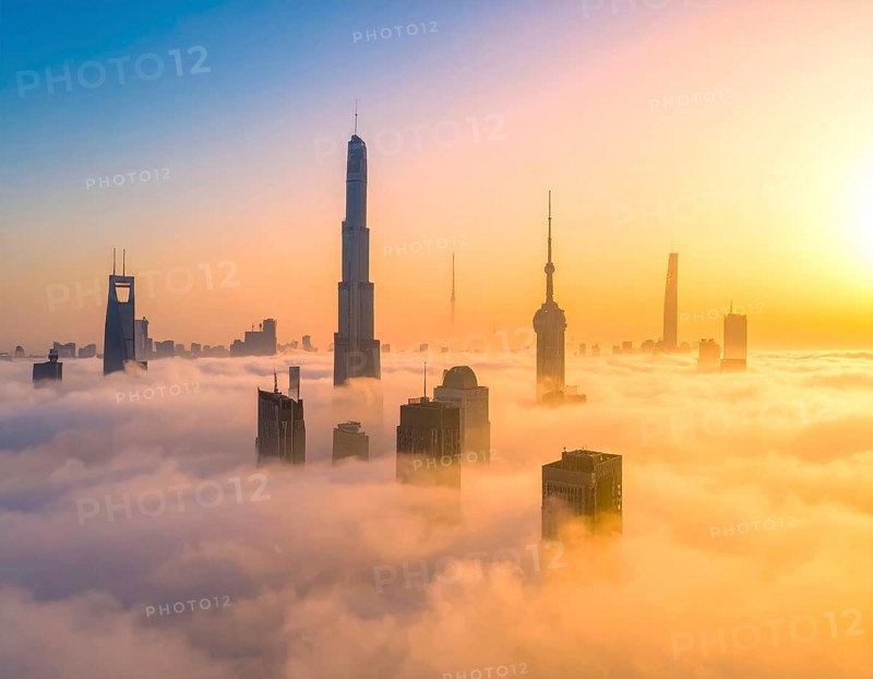 City scape emerging from a dense enveloping fog in sunrise and skyscrapers piercing the haze, big metropolis with skyline, mist on ground, blue sky, city in an aerial view, AI generated