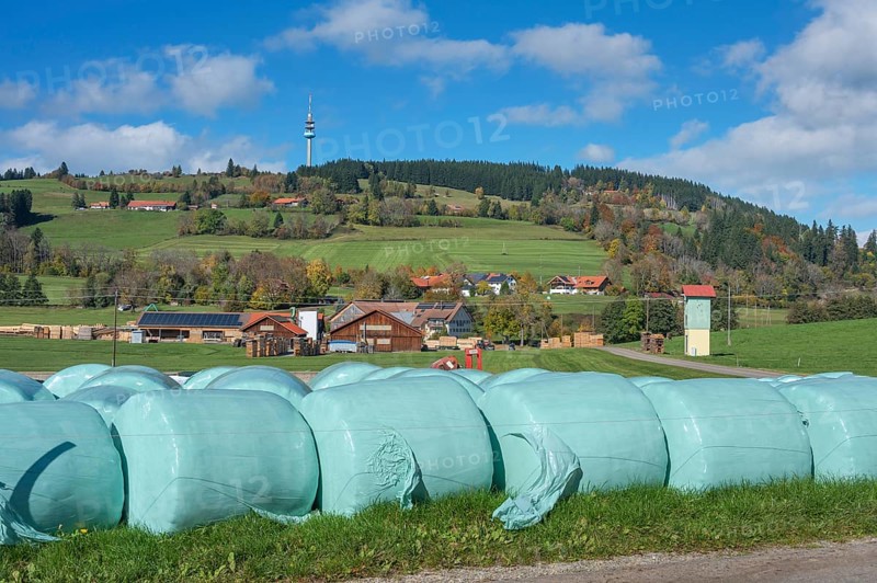Blue sky with clouds, silage bales in front of the village of Masers under the mountain Blender with telecommunications tower near Kempten, Swabia, Bavaria, Germany