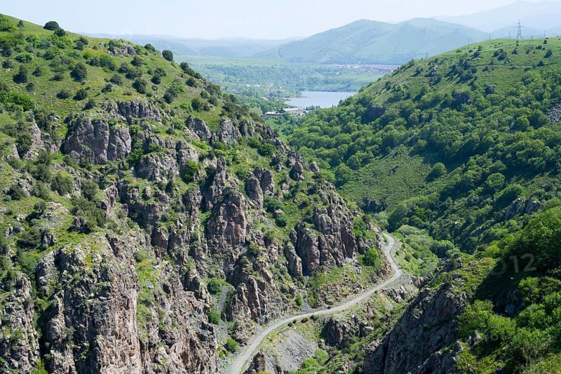A green mountain landscape with rocks crossed by a road with a wide view of the valley, canyon of the Arpa River, in the background the Kechut Reservoir, Kushchi, Kush-Bilyak, Wajoz Dzor Province, Vayots Dzor, Armenia