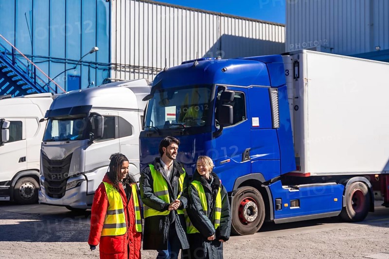 Logistics team in high visibility winter gear consulting by refrigerated trucks at a warehouse loading dock, coordinating frozen goods transport and cold storage operations