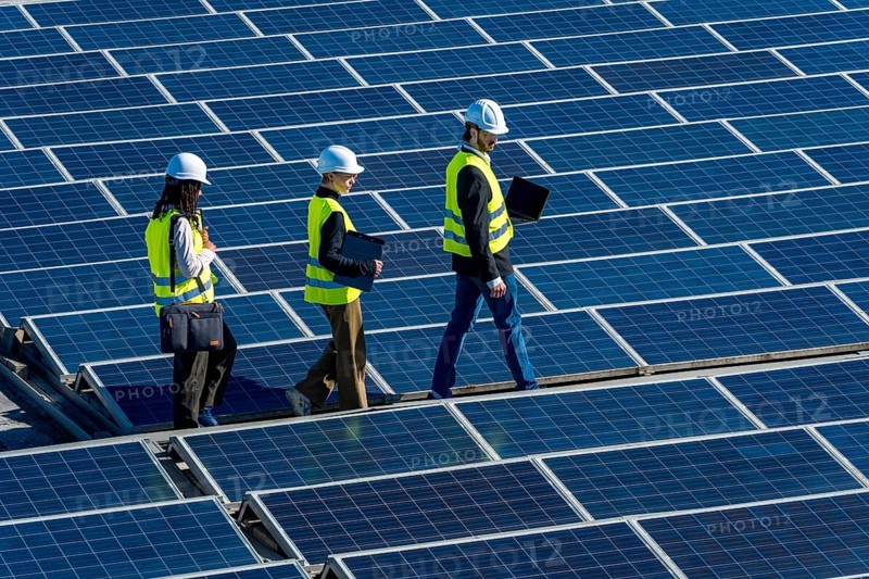 Engineers in hard hats and vests walking on a large solar panel array, inspecting the installation and ensuring the efficiency of the clean energy production system