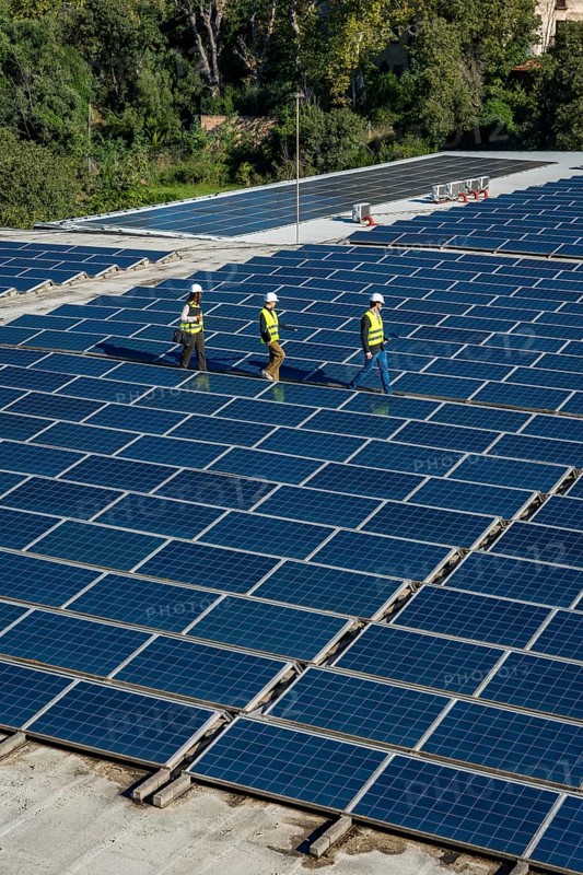 Engineers wearing safety gear are walking along rows of extensive solar panels on a rooftop, symbolizing sustainable development and renewable energy production