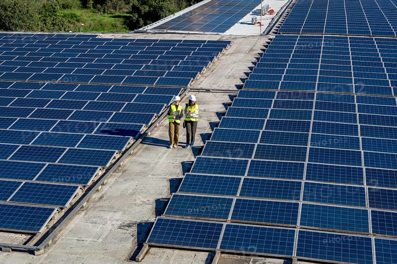 Engineers in hard hats and vests performing an inspection of a rooftop solar power plant, ensuring the efficiency and sustainability of renewable energy production