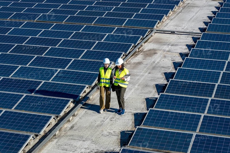 Two engineers, a man and a woman, are working outdoors, reviewing plans and inspecting rows of solar panels on a large rooftop array, embodying renewable energy and sustainability