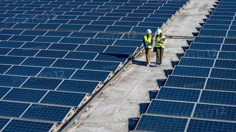 Two engineers wearing hard hats and safety vests walking on a rooftop solar farm, planning installation or performing maintenance on renewable energy power generation system