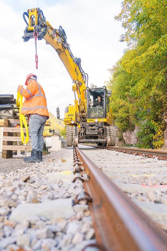 Excavator working on track, construction worker checking equipment, focus on rails, autumn landscape, signal construction at Hermann Hessebahn, Calw, Germany