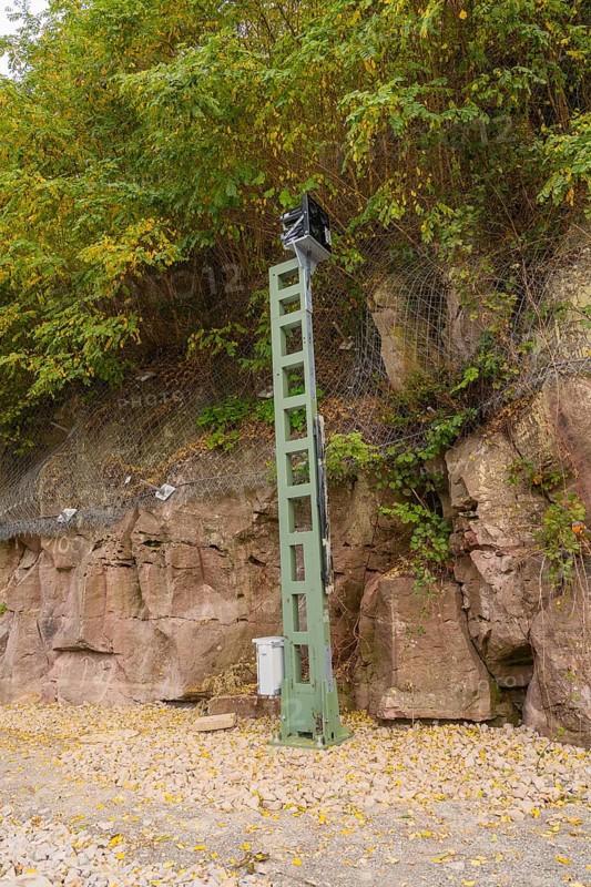 Green signal tower in front of rocky embankment with trees and safety net, Signalbau an der Hermann Hessebahn, Calw, Germany