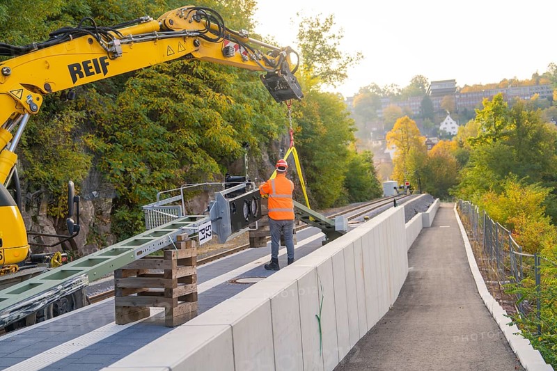 Track work with excavator, construction worker fixing objects, autumn urban landscape, signal construction on the Hermann Hessebahn, Calw, Germany
