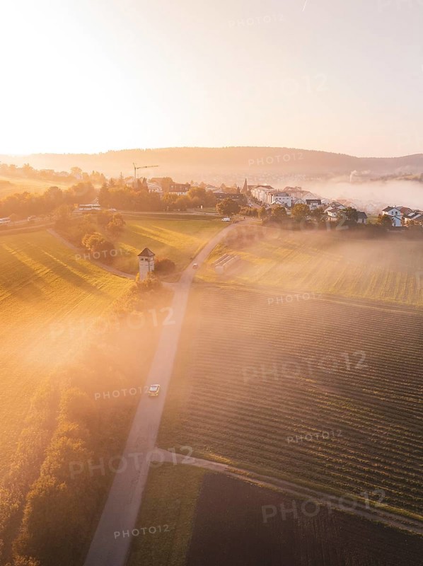 Fields and a village with a tower, wrapped in fog and illuminated by soft morning light, Calw Stammheim, Black Forest, Germany