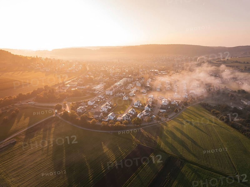 A village surrounded by fields in fog at sunrise with warm orange light, Calw Stammheim, Black Forest, Germany
