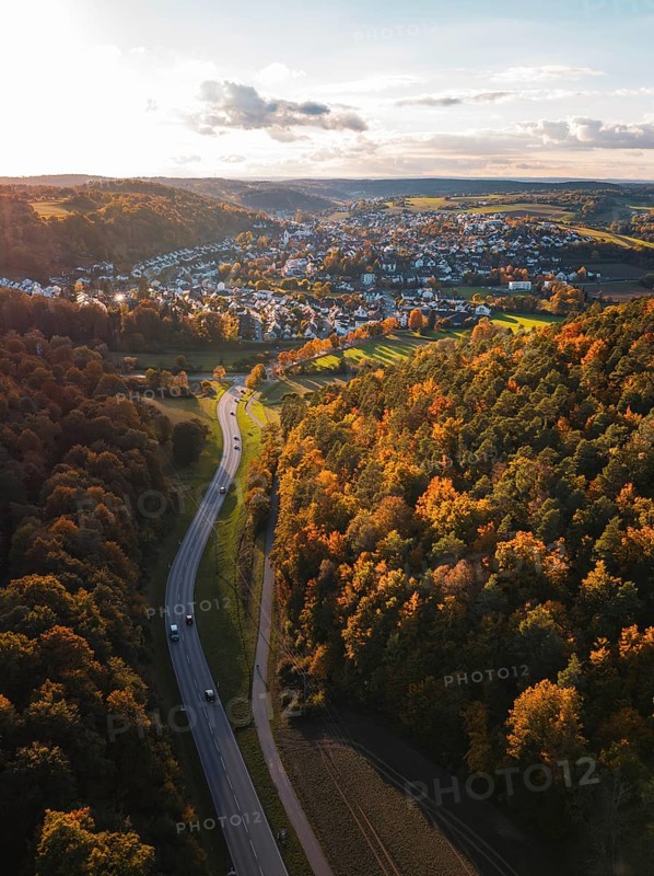 A road snakes through autumn trees towards a small village, Aidlingen, Böblingen district, Germany