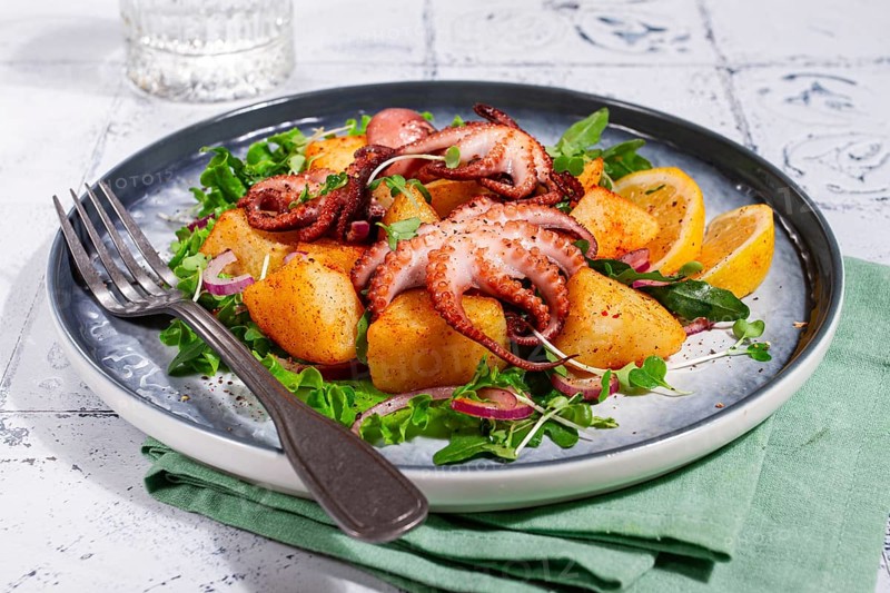 Warm grilled octopus salad with potatoes and fresh herbs, on a stylish plate, homemade