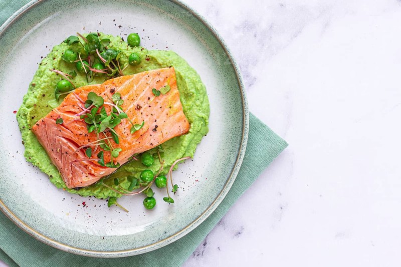 Delicious grilled salmon is placed elegantly on creamy green pea puree. Fresh microgreens and peas add a bright touch, creating an appetizing dish perfect for any meal