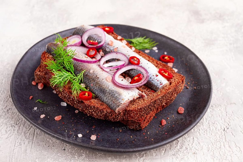 Sandwiches, herring fish, on dark rye bread, sprinkled with onion, chili pepper and herbs, on a dark plate