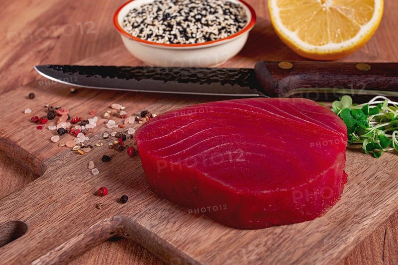 Fresh tuna steak, on a wooden cutting board, with lemon and sesame seeds, on a wooden table