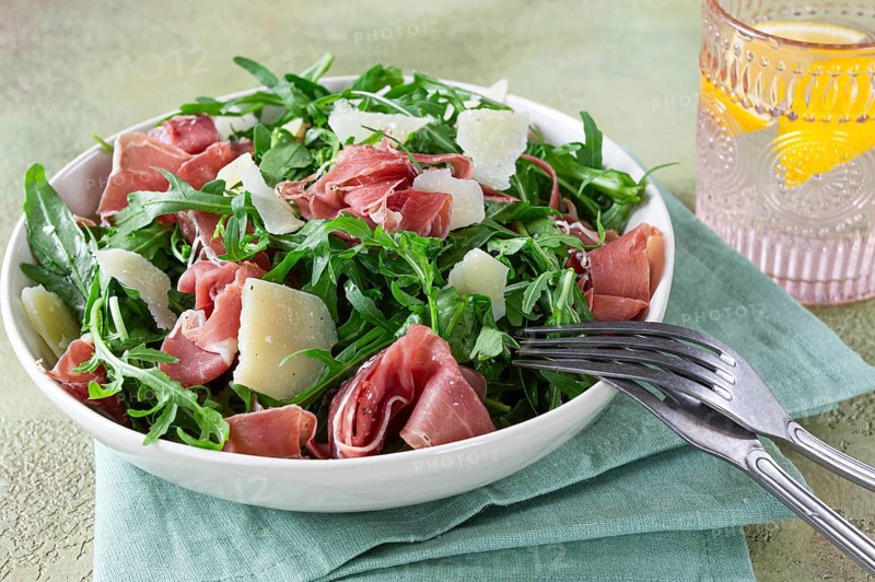 Fresh arugula salad with prosciutto and grated parmesan cheese, on a plate, homemade, no people