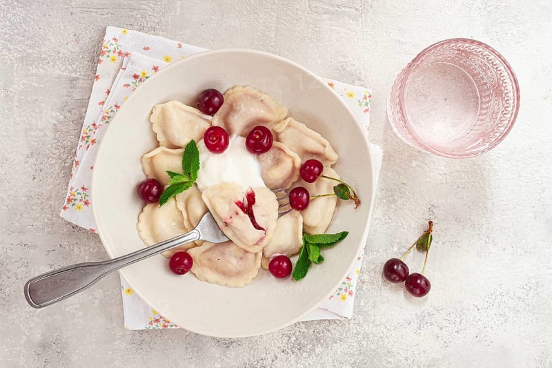Traditional dumplings with cherries and yogurt, in a bowl, light background, close-up, no people
