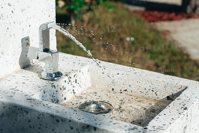 A clean tap fountain dispenses fresh water in a park surrounded by greenery. Sunlight shines on the water, creating a refreshing atmosphere for visitors enjoying the outdoors