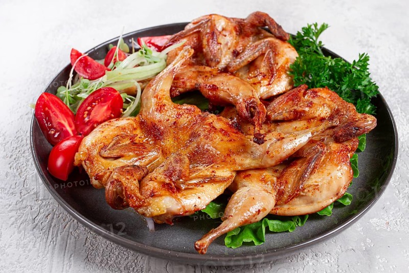 Baked quail, served on a plate with crispy lettuce leaves, fresh tomatoes and herbs, on a dark plate, homemade