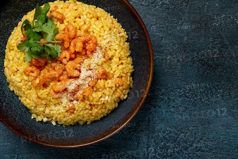 Risotto with shrimp, in a bowl, on a textured surface, with a side dish of fresh coriander, homemade, no people