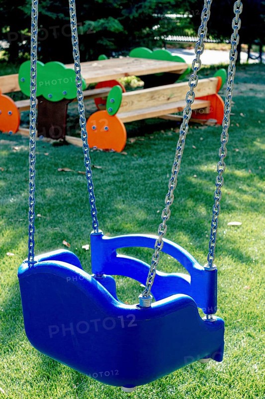 A bright blue swing hangs from sturdy chains in a lively playground. The well-maintained area features green grass and colorful benches, perfect for children to play and relax