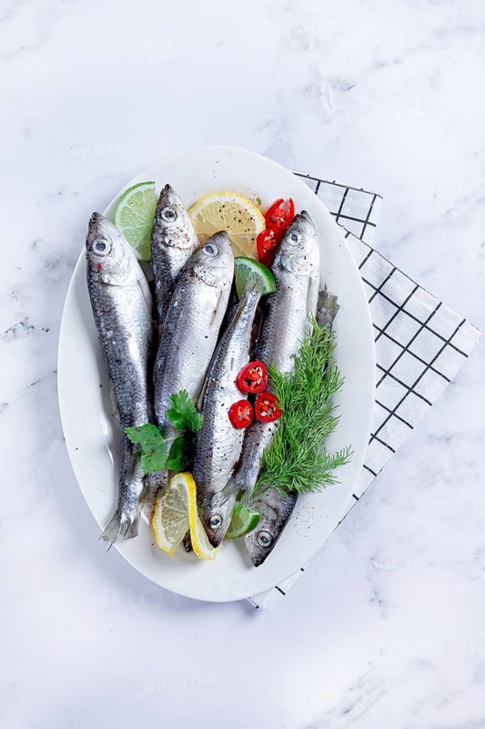 Fresh Herring fish, ready to cook, with herbs and spices, on a white platter, in the kitchen