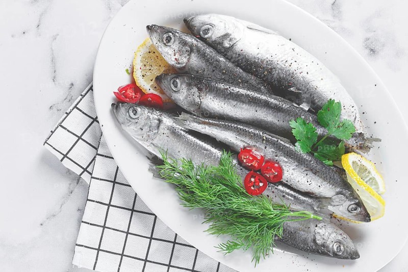 Fresh Herring fish, ready to cook, with herbs and spices, on a white platter, in the kitchen