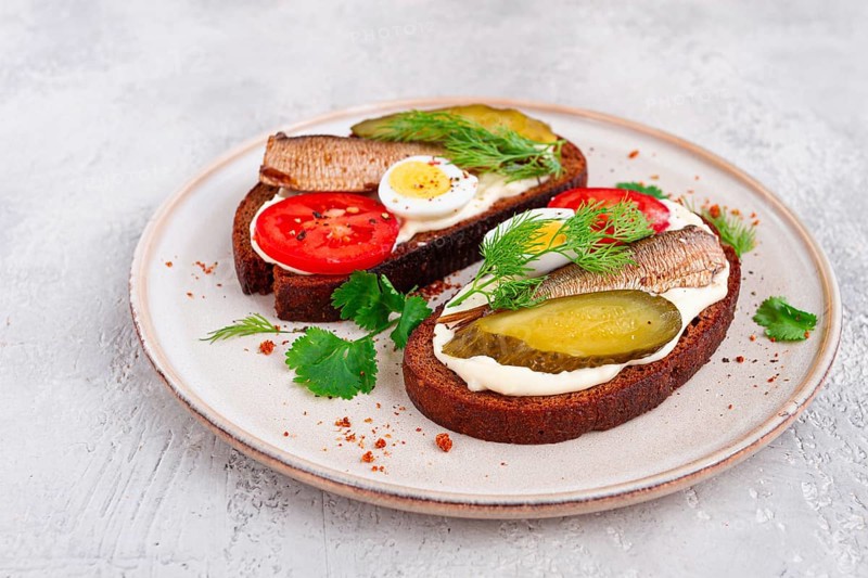 Sandwiches on rye bread, with sprats, quail eggs, fresh tomatoes and pickled cucumber, appetizer, breakfast, homemade